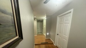 Un couloir avec un plancher en bois, une porte blanche et un tableau encadré accroché au mur.