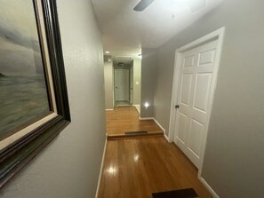 A hallway with wooden flooring, a white door, and a framed picture on the wall.