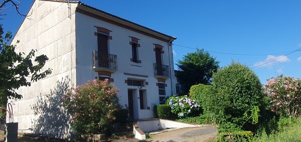 A two-story building with a white facade, a balcony on the second floor, and a small front porch.