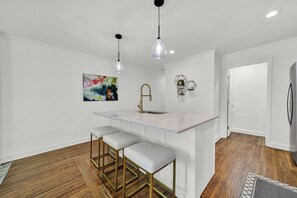 A modern kitchen with a central island, bar stools, pendant lighting, and a colorful abstract painting. - Duplex by Uptown (Charlotte)