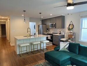A modern kitchen with a central island, bar stools, and a ceiling fan. - Duplex by Uptown (Charlotte)