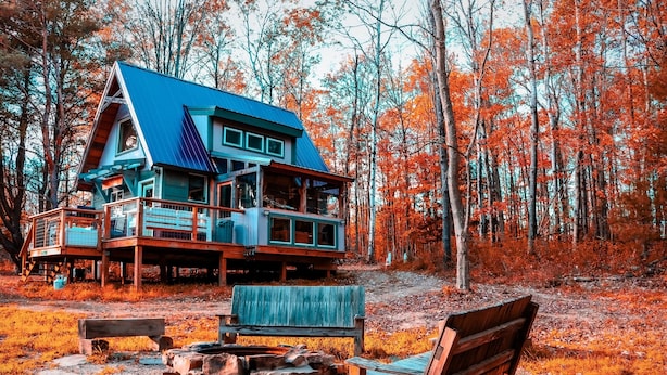 Una baita dal tetto blu e veranda in legno, circondata da alberi autunnali.