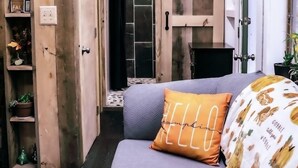 Una stanza accogliente con arredamento in legno, un divano grigio con un cuscino che riporta la scritta 'HELLO' e un letto con copripiumino floreale.