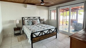 A bedroom with a wooden ceiling, a bed with a metal frame, a nightstand, a lamp, and a view through a glass door to an outdoor area. - BEACHFRONT CASITA Snorkel & explore this amazing reef~ Experience Caribbean Life (Sandy Bay)