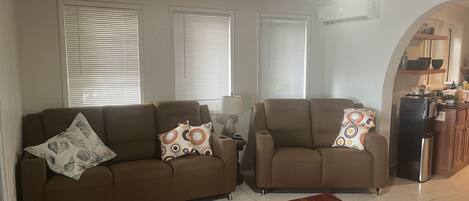 A living room with two sofas, a rug, and a kitchen area visible through an archway.