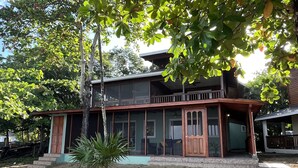 A two-story building with a balcony, surrounded by trees and a sandy ground. - BEACHFRONT CASITA Snorkel & explore this amazing reef~ Experience Caribbean Life (Sandy Bay)