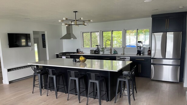 Una cocina moderna con una isla grande, taburetes de bar, electrodomésticos de acero inoxidable y un televisor montado en la pared.