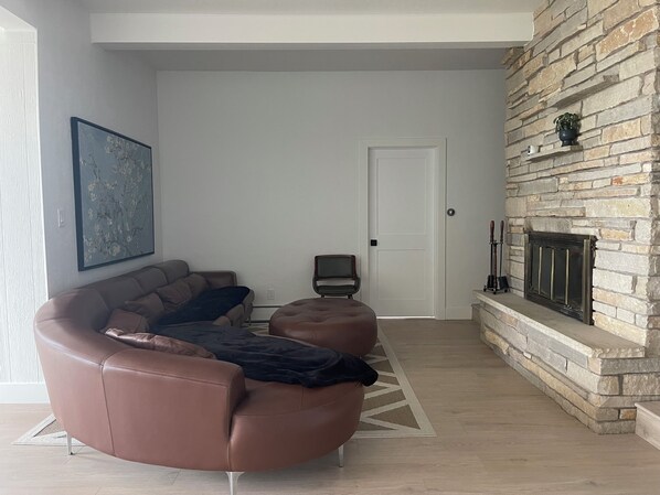 A living room with a stone fireplace, a brown leather sofa, a black armchair, and a large abstract painting on the wall.