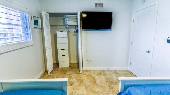 A bedroom with a bed, a closet, a television, and a window with blinds.
