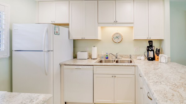 Una cocina con refrigerador, tostadora, pileta y cafetera.