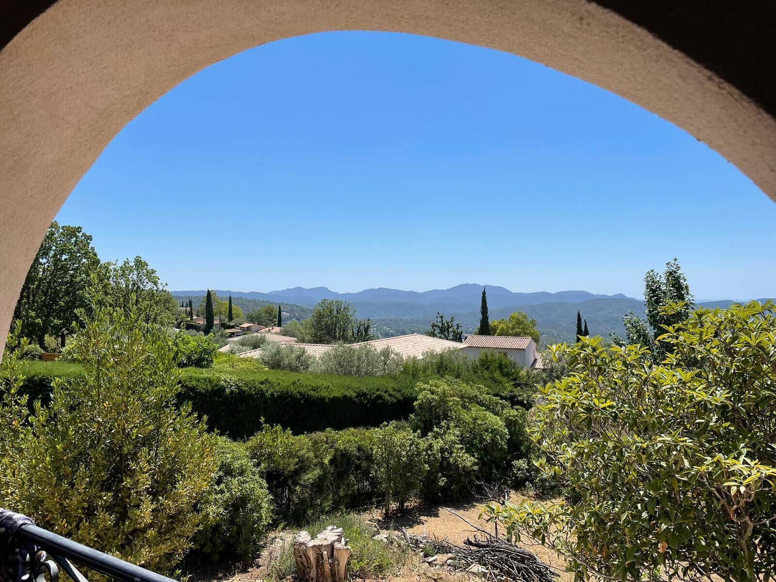 Une vue à travers une fenêtre circulaire sur un paysage rural, avec des collines ondoyantes et des bâtiments dispersés.