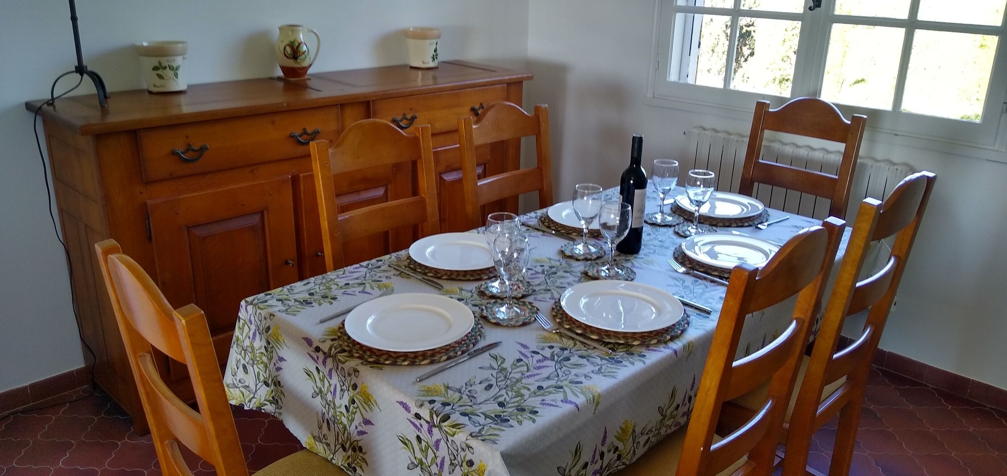 A dining table set with plates, glasses, and a wine bottle, surrounded by wooden chairs.