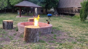 Ein Garten mit einem runden Feuerkorb, einem hölzernen Baumstumpf und einem Gartenpavillon.