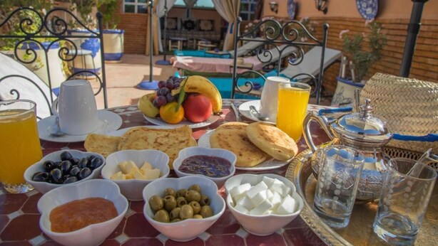 A breakfast table with various food items, a glass of orange juice, and a teapot. - 66 Av. Imam El Ghazali (Marrakech)