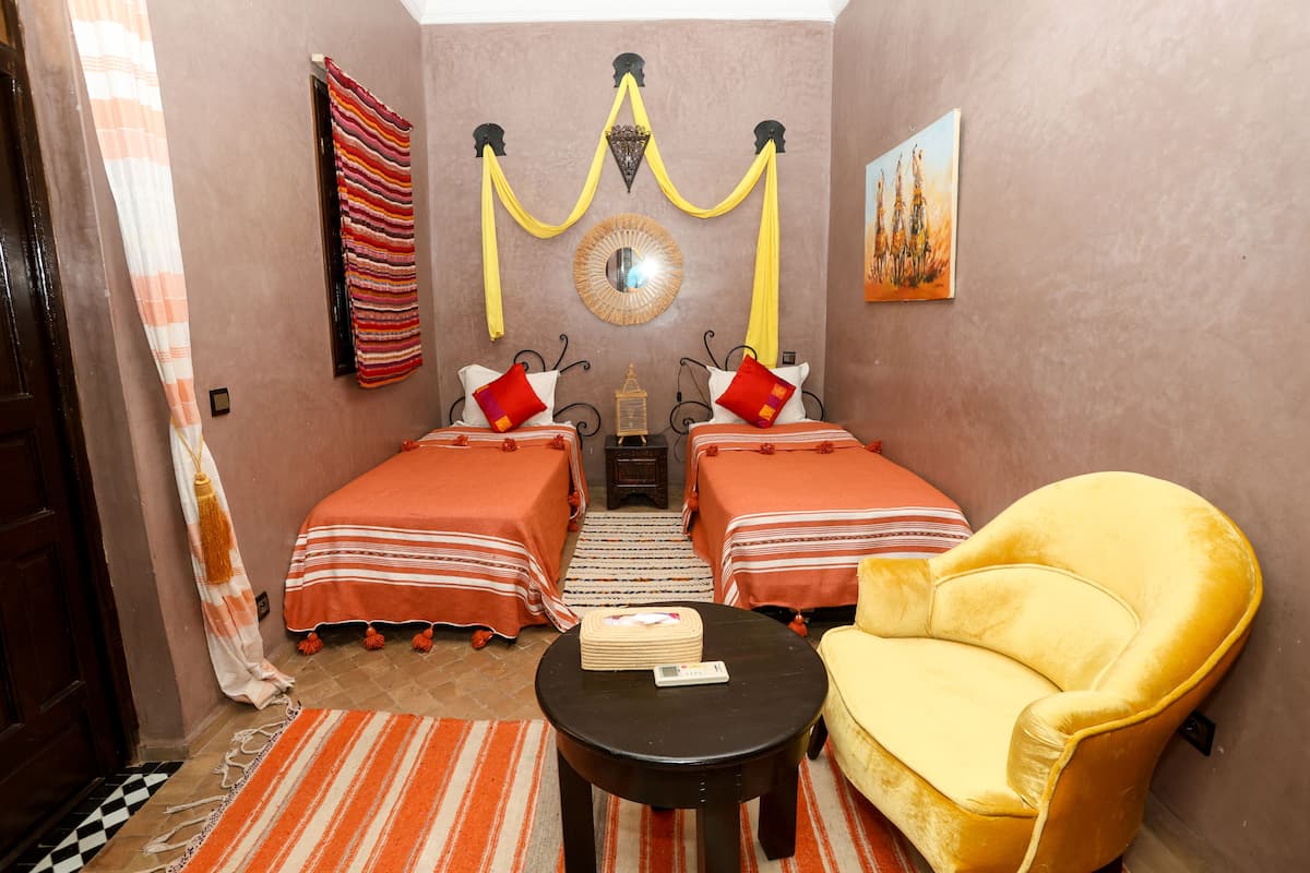 A room with two beds, a yellow armchair, a small table, and a decorative mirror on the wall.