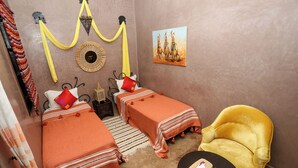 A room with two beds, a yellow armchair, a round table, and a painting on the wall. - 66 Av. Imam El Ghazali (Marrakech)