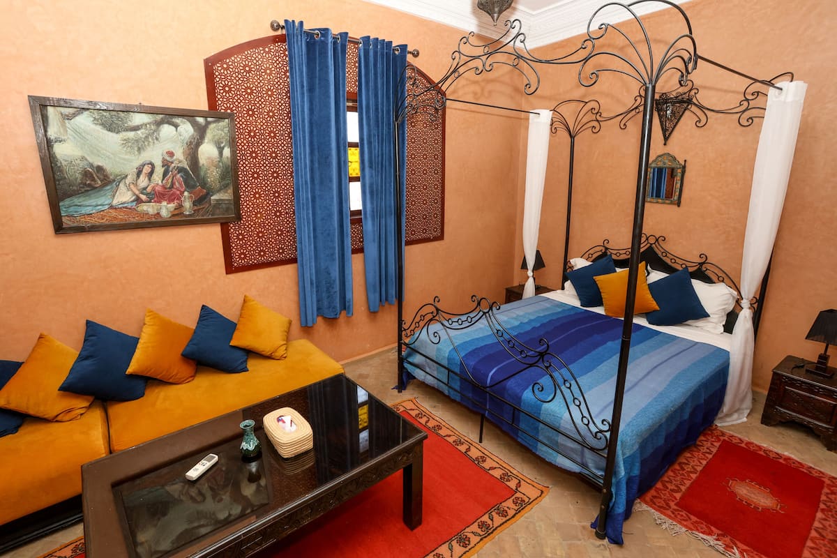 A bedroom with a bed, a sofa, a coffee table, and a painting on the wall.