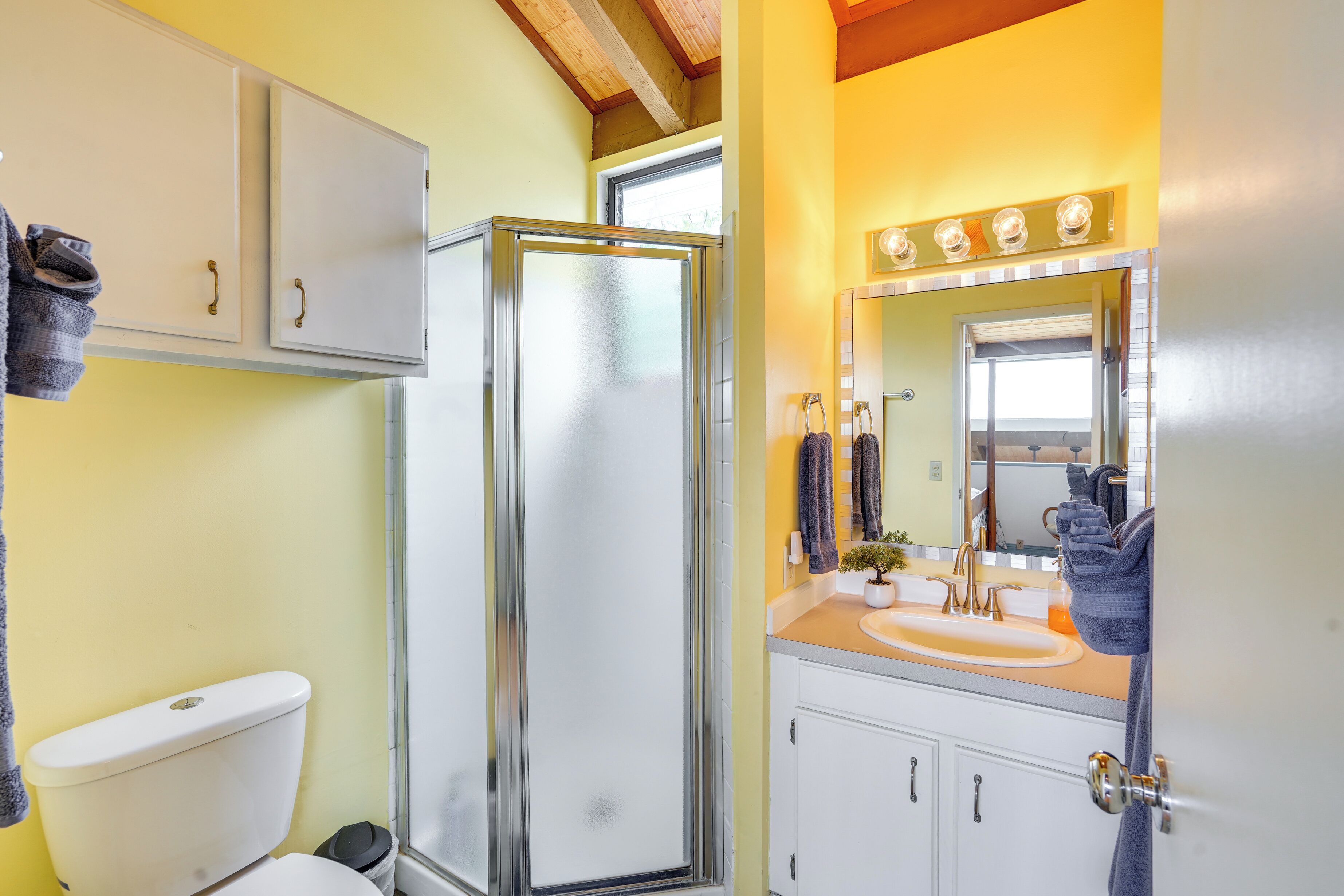 A bathroom with a toilet, a shower enclosure, a sink with a mirror, and cabinets.