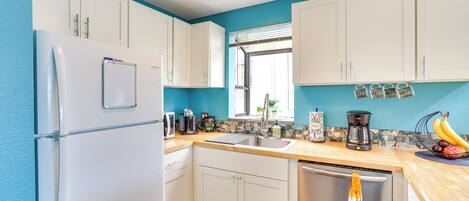 A kitchen with white cabinets, a stainless steel refrigerator, a coffee maker, and a dish rack.