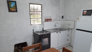 A compact kitchen with white cabinets, a stove, oven, and a refrigerator. There's a window with a view of trees and a painting on the wall.