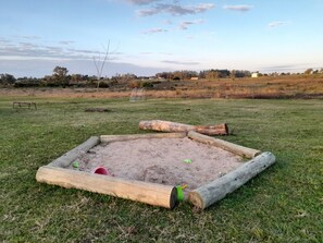 Un bac à sable avec des bordures en bois et un banc dans un champ d’herbe.