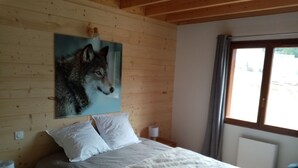 A bedroom with a wooden ceiling, a large painting of a wolf, a bed with white bedding, and a window with curtains.
