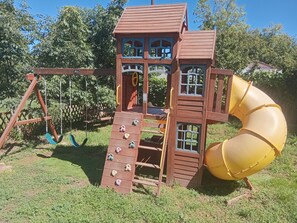 A wooden play structure with a slide and climbing steps.