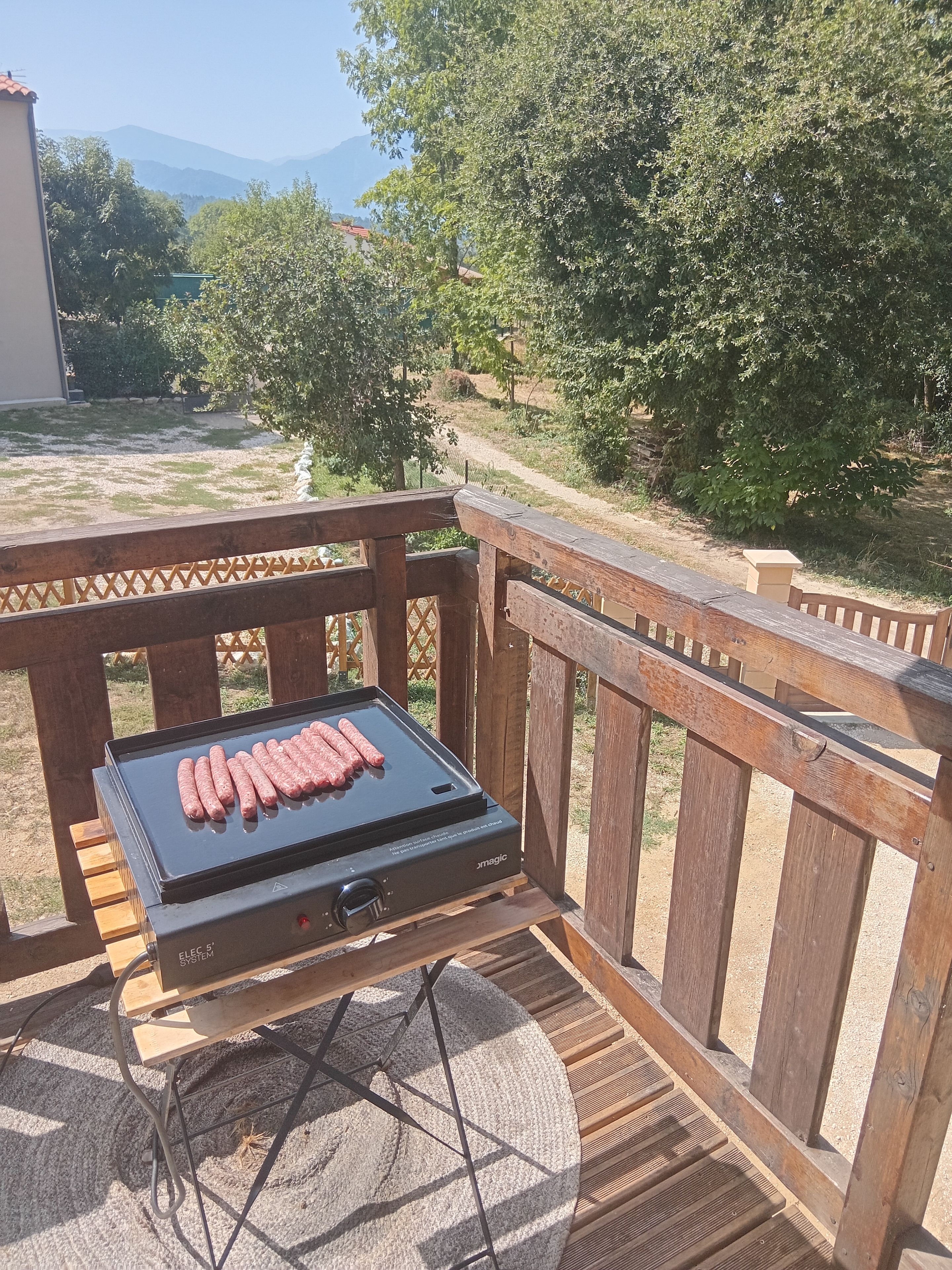 Grilli, jossa on makkaroita, on sijoitettu puukannelle, jolta avautuu näkymä puihin ja vuorille.