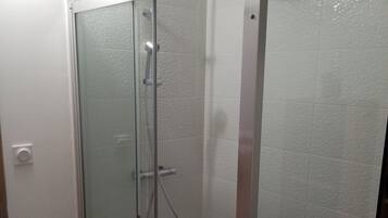 A glass-enclosed shower stall with a handheld showerhead and a wall-mounted faucet.