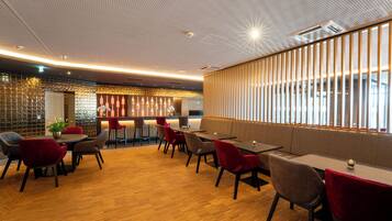 Un restaurante moderno con suelo de madera, sillas rojas y grises, y una zona de bar con una pared decorativa.
