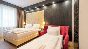 A hotel room with two beds, a large headboard, and a nightstand with lamps.