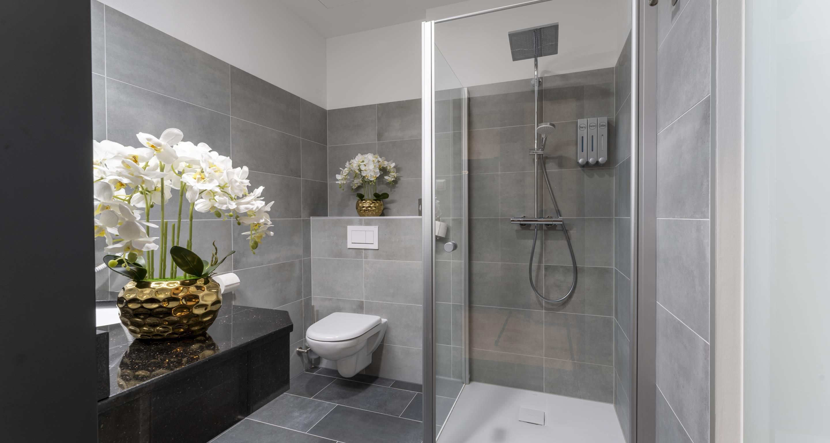 A modern bathroom with a shower, toilet, and a decorative vase with flowers.