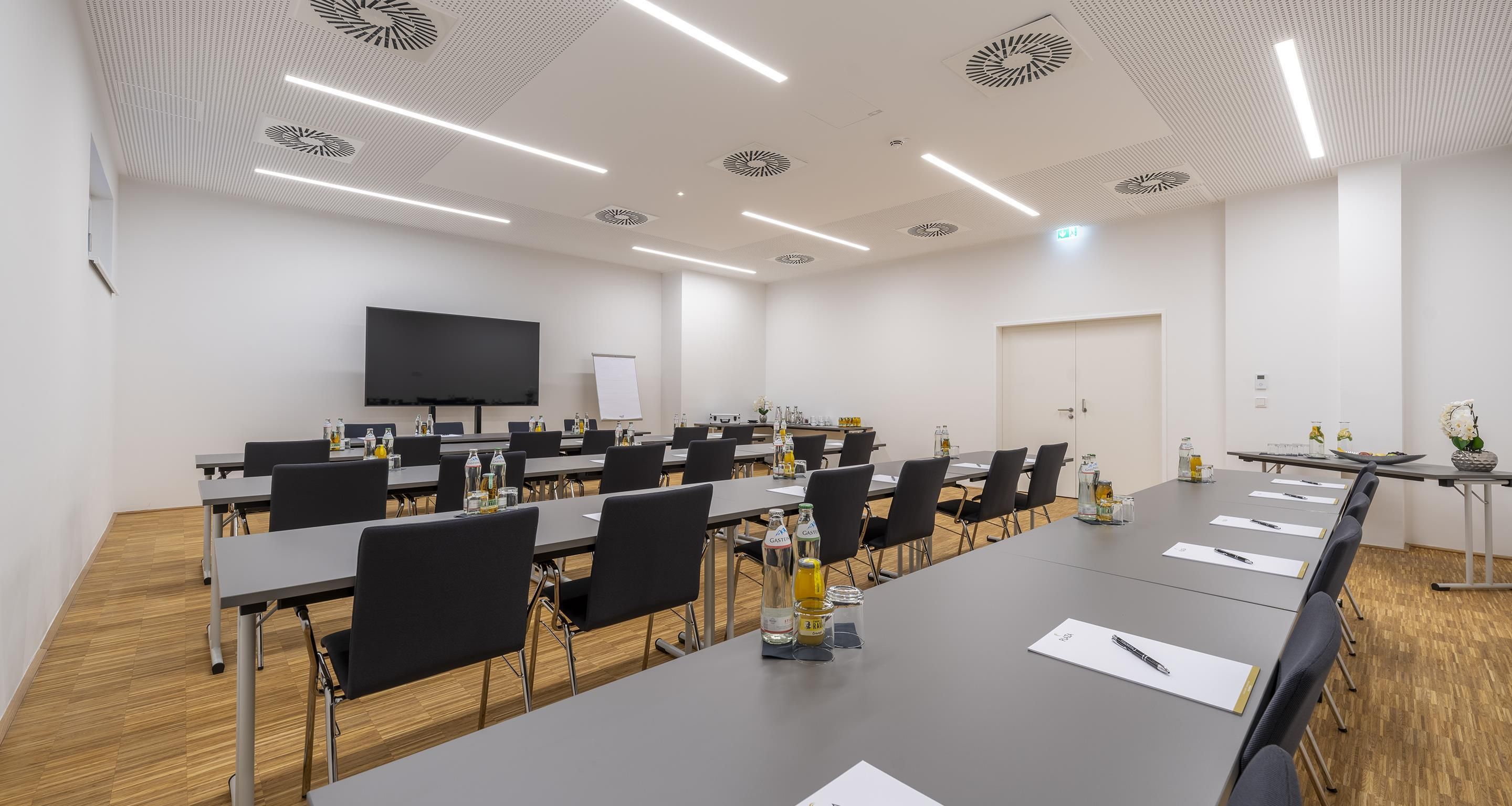 Uma sala de conferência com uma mesa comprida, cadeiras, uma tela de projetor e um quadro branco.