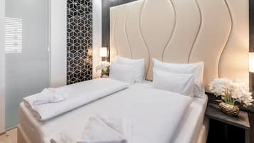 A neatly made bed with white linens and pillows, a decorative wall with a geometric pattern, and a small table with a vase of flowers.