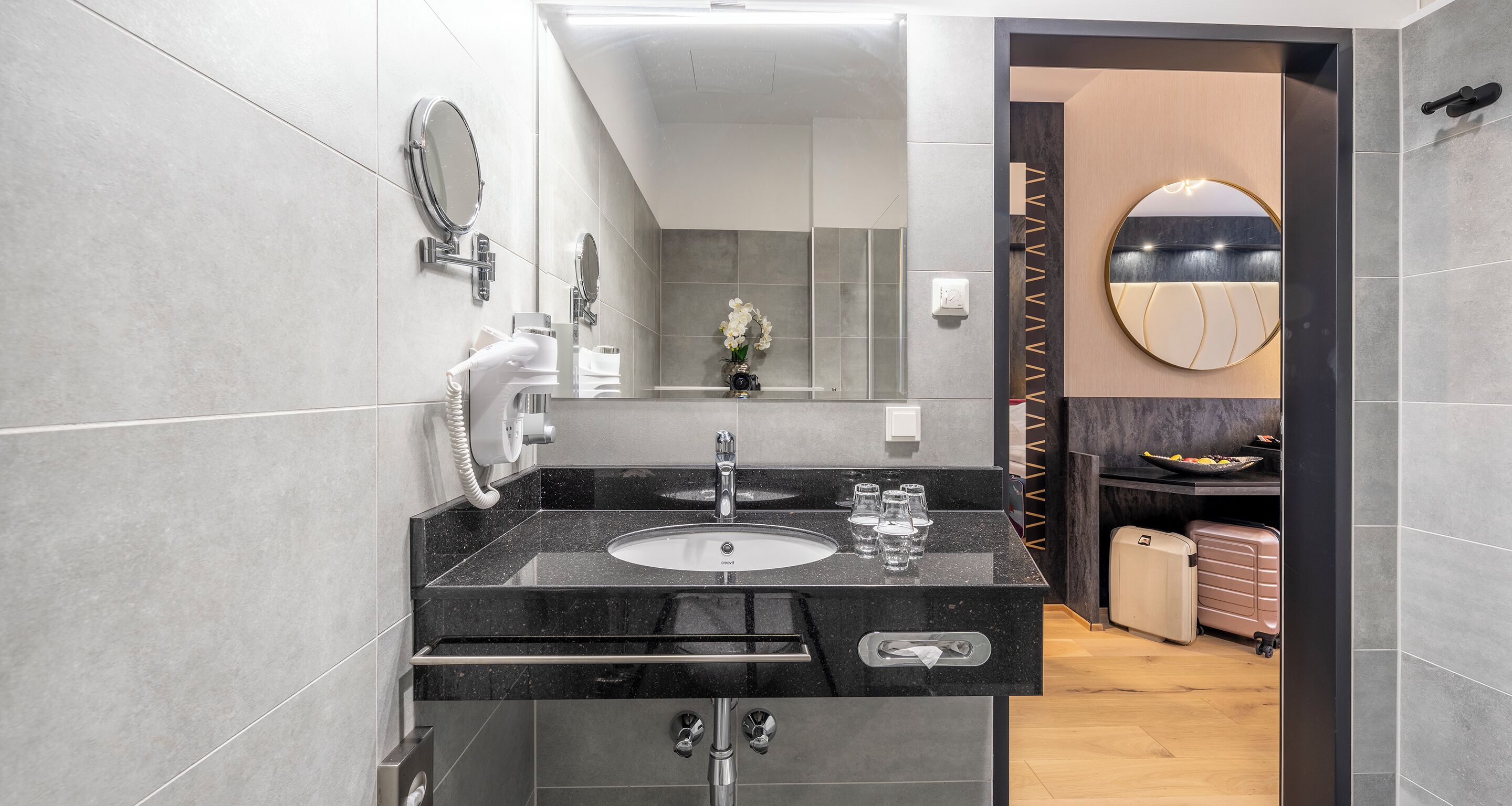 A modern bathroom with a black granite sink, two mirrors, and a towel rack.
