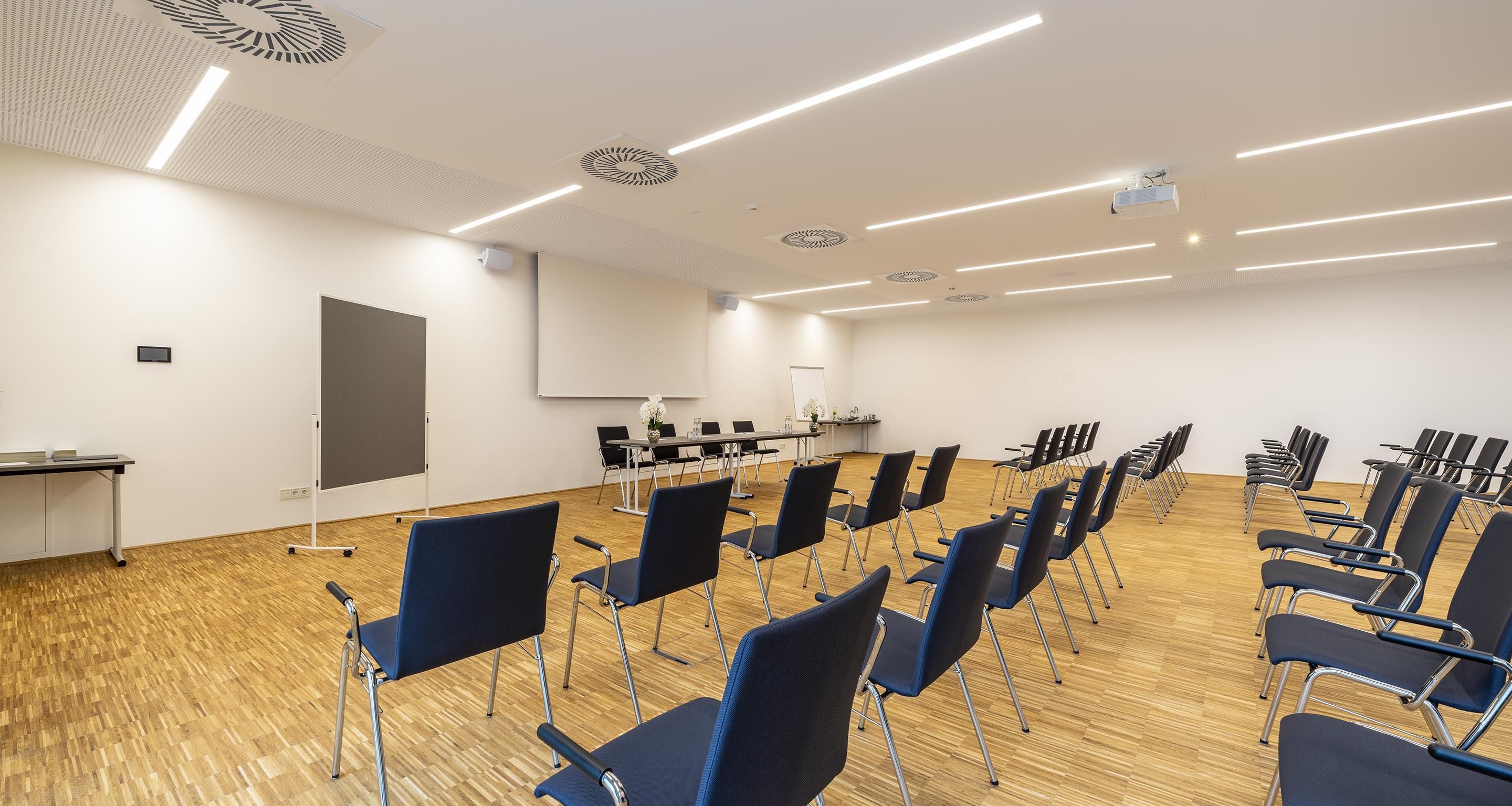 Una sala de conferencias con filas de sillas, una pantalla de proyector y una pizarra.