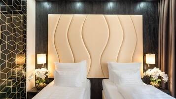 A hotel room with a large, cushioned headboard, two beds with white linens, bedside lamps, and a decorative wall panel.