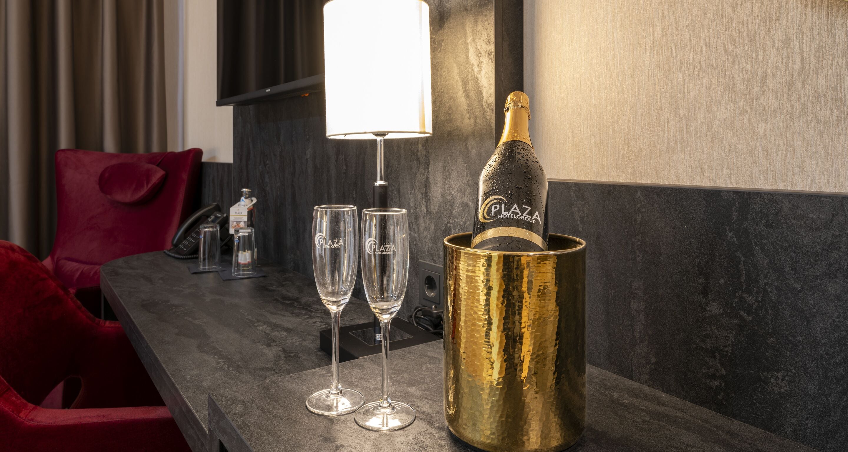 Una habitación con una mesa de madera oscura, dos copas de champán, un cubo dorado para champán y una lámpara blanca.