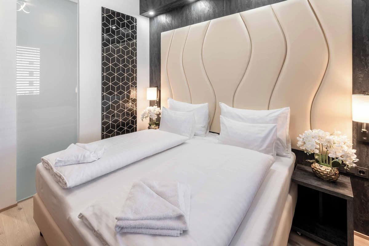 Ein Hotelzimmer mit einem großen Bett, einem Nachttisch mit Lampe, einer dekorativen Wandverkleidung und einer Tür mit Milchglas.
