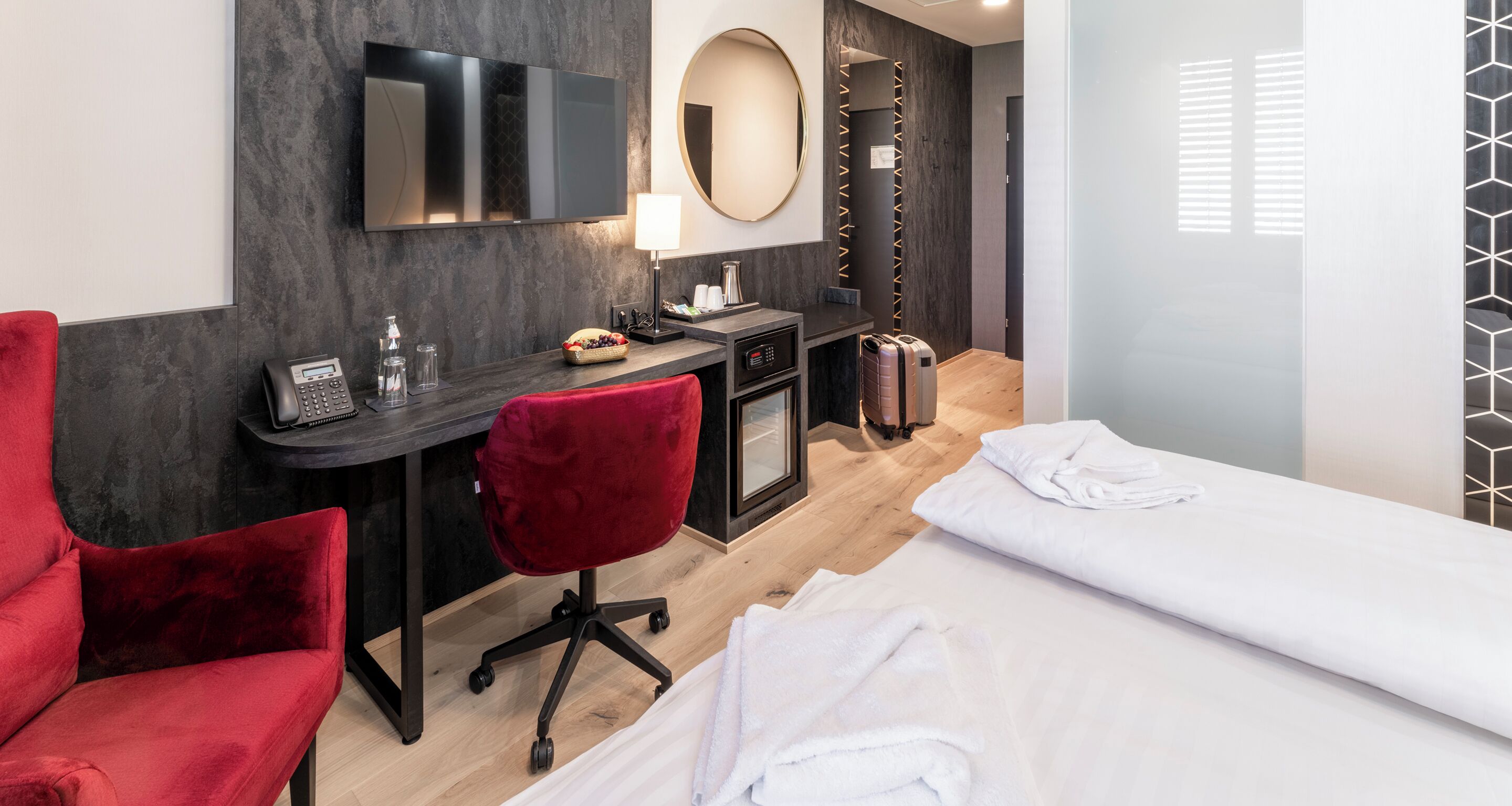 A hotel room with a desk, red chair, and a bed.