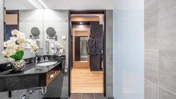 Un baño moderno con encimera negra, un espejo redondo, toallero y zona de ducha visible a través de una puerta abierta.