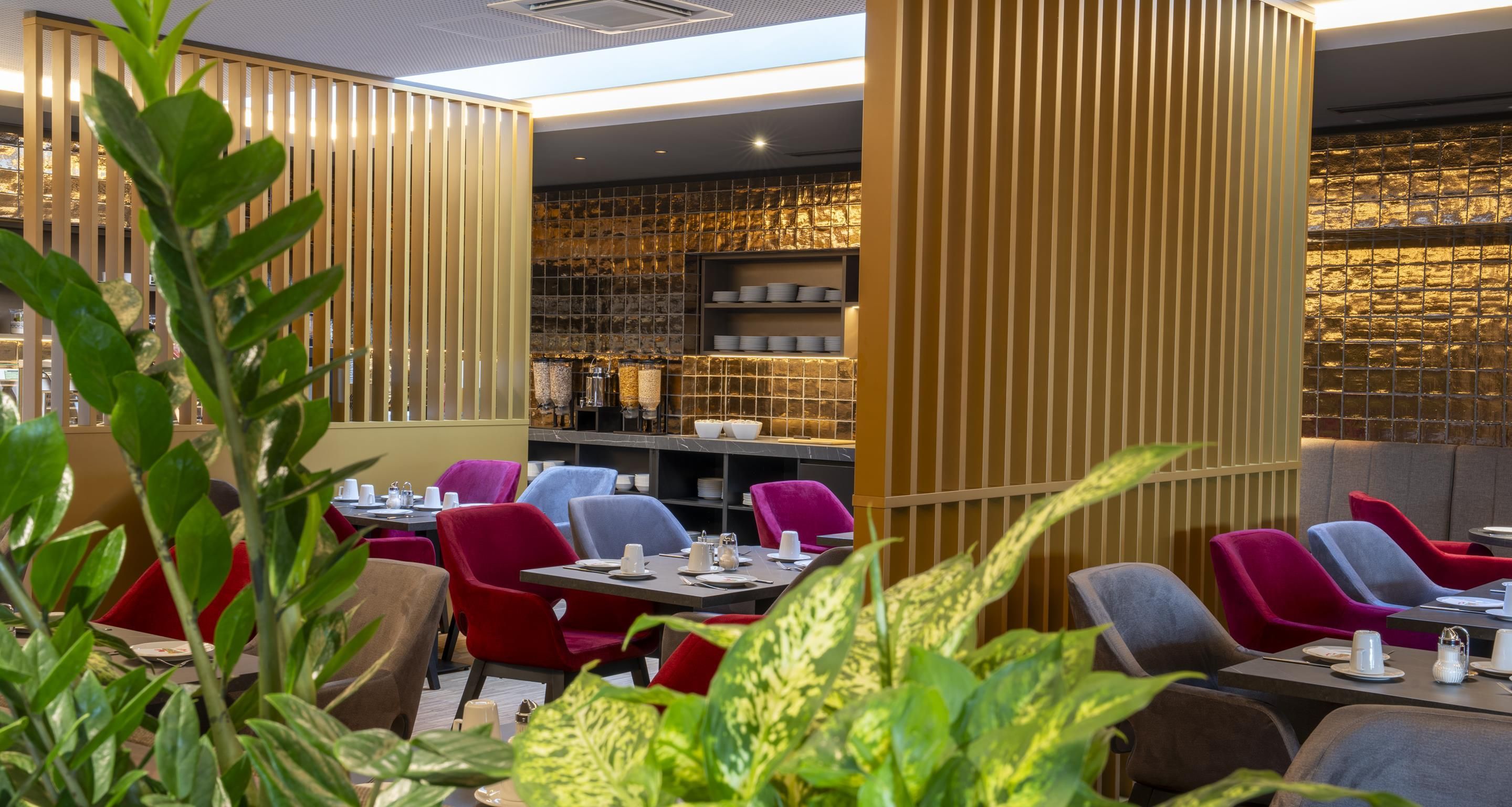 A restaurant interior with high tables, red and grey chairs, and a bar area with shelves.