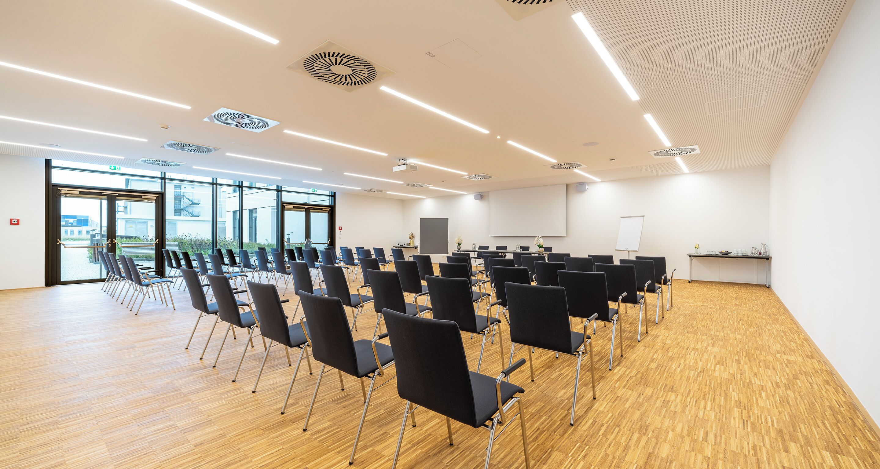 Una sala de conferencias con filas de sillas, una pizarra y una pantalla de proyector.