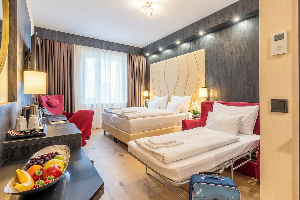 Ein Hotelzimmer mit zwei Betten, einem Schreibtisch mit Obstschale, einem roten Sessel und einem Spiegel.