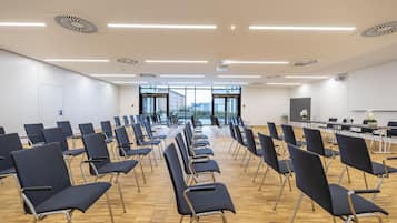 Un salón de conferencias con filas de sillas, una mesa grande y una pantalla de proyector.