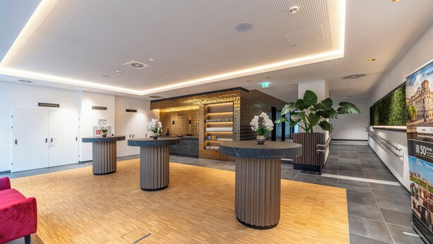A modern hotel lobby with a reception desk, seating area, and a large poster on the wall. - PLAZA INN Wiener Neustadt, BW Signature Collection (Wiener Neustadt)