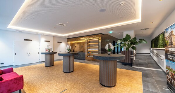 A modern hotel lobby with a reception desk, seating area, and a large poster on the wall. - PLAZA INN Wiener Neustadt, BW Signature Collection (Wiener Neustadt)