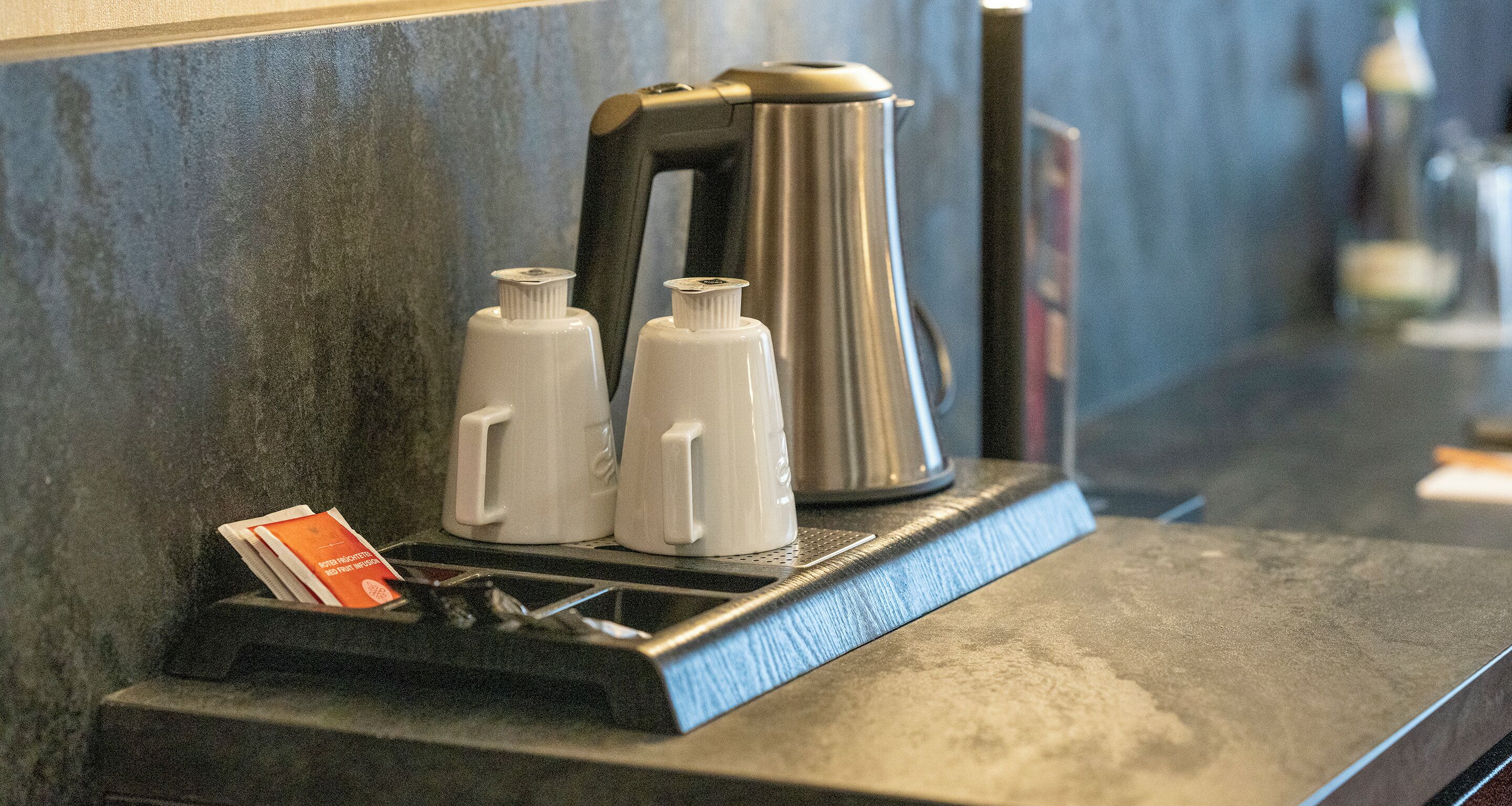 A countertop with a coffee maker, two white bottles, and a tray with a card.