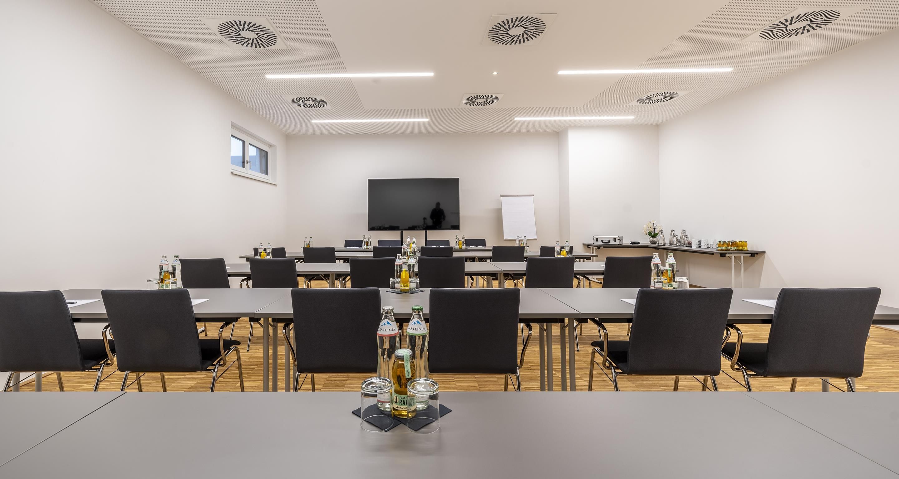 Una sala de conferencias con una larga mesa, sillas, una pizarra y una pantalla de televisión.