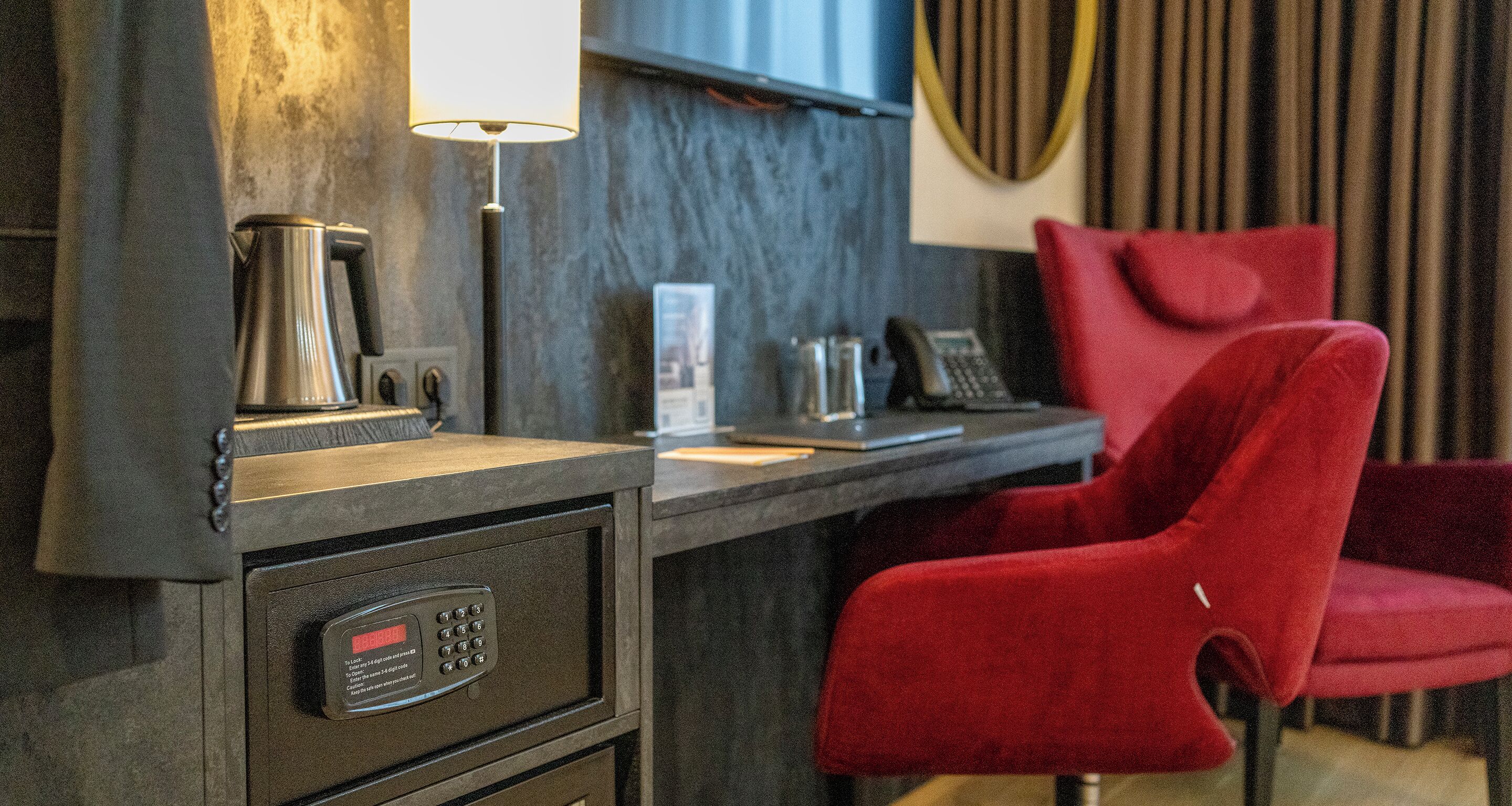 Ein modernes Hotelzimmer mit einem dunklen Holztisch, einem roten Sessel, einer Kaffeemaschine und einem Telefon.